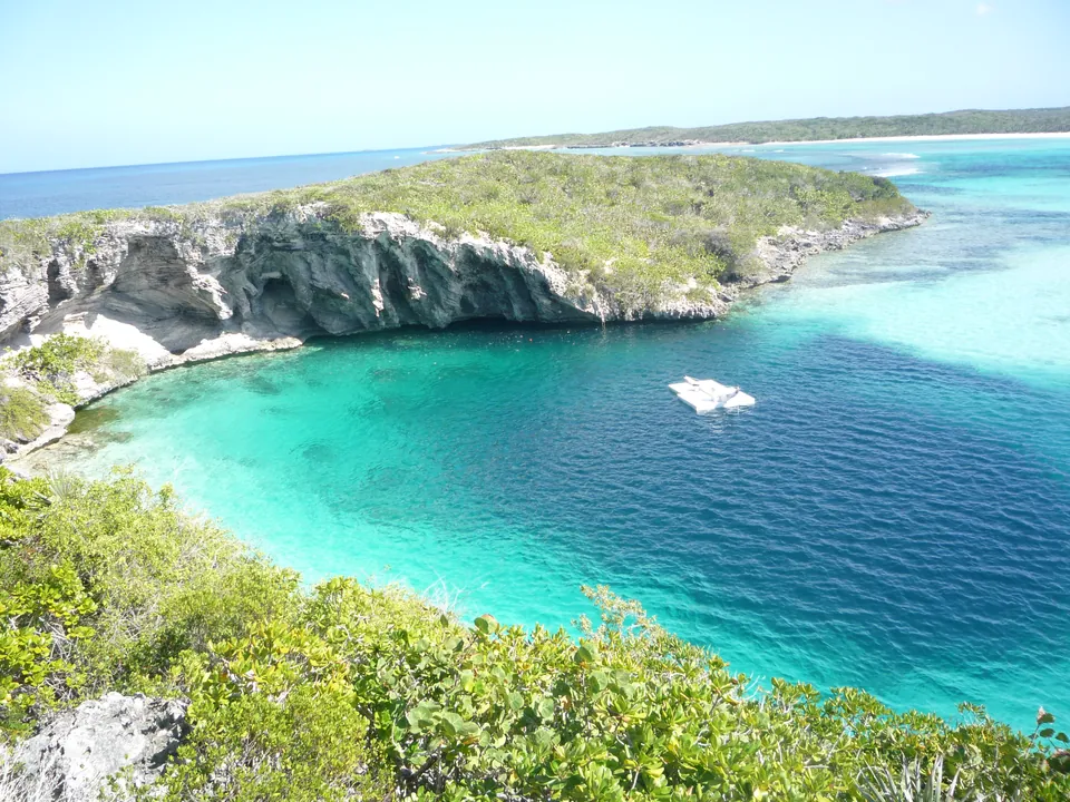 Dean's Blue Hole na Bahamach: granatowe oko wody w turkusowej zatoce pod wapiennym klifem porośniętym zielenią, na wodzie biała platforma freediverów - zdjęcie poglądowe