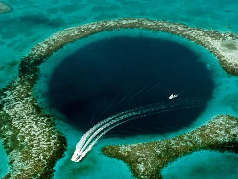 Great Blue Hole z lotu ptaka: ciemnogranatowy okrągły otwór wśród turkusowej rafy, łódź na powierzchni - zdjęcie poglądowe