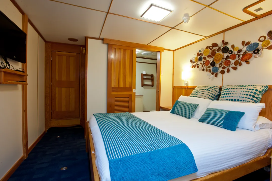 Kabina stateroom z podwójnym łóżkiem i telewizorem na ścianie